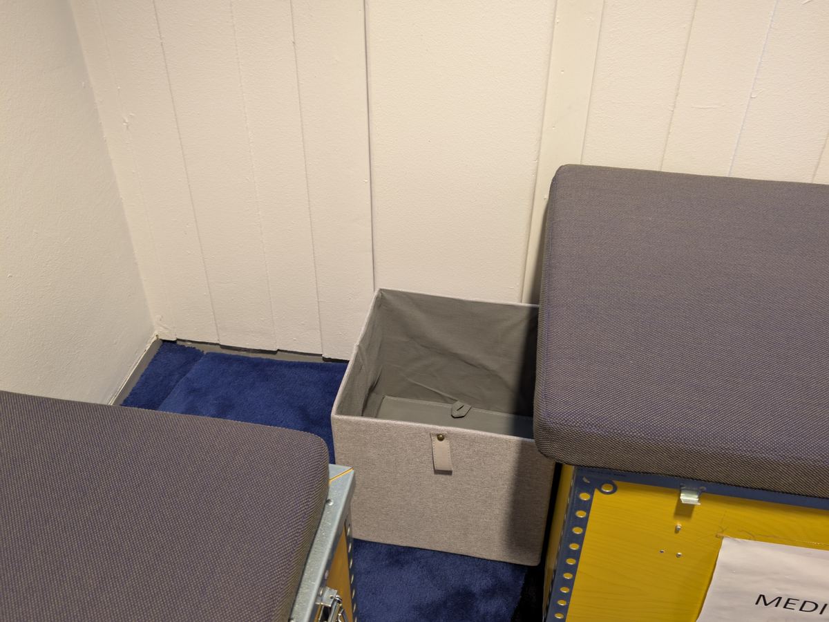 The box is grey fabric, on the floor between two benches.